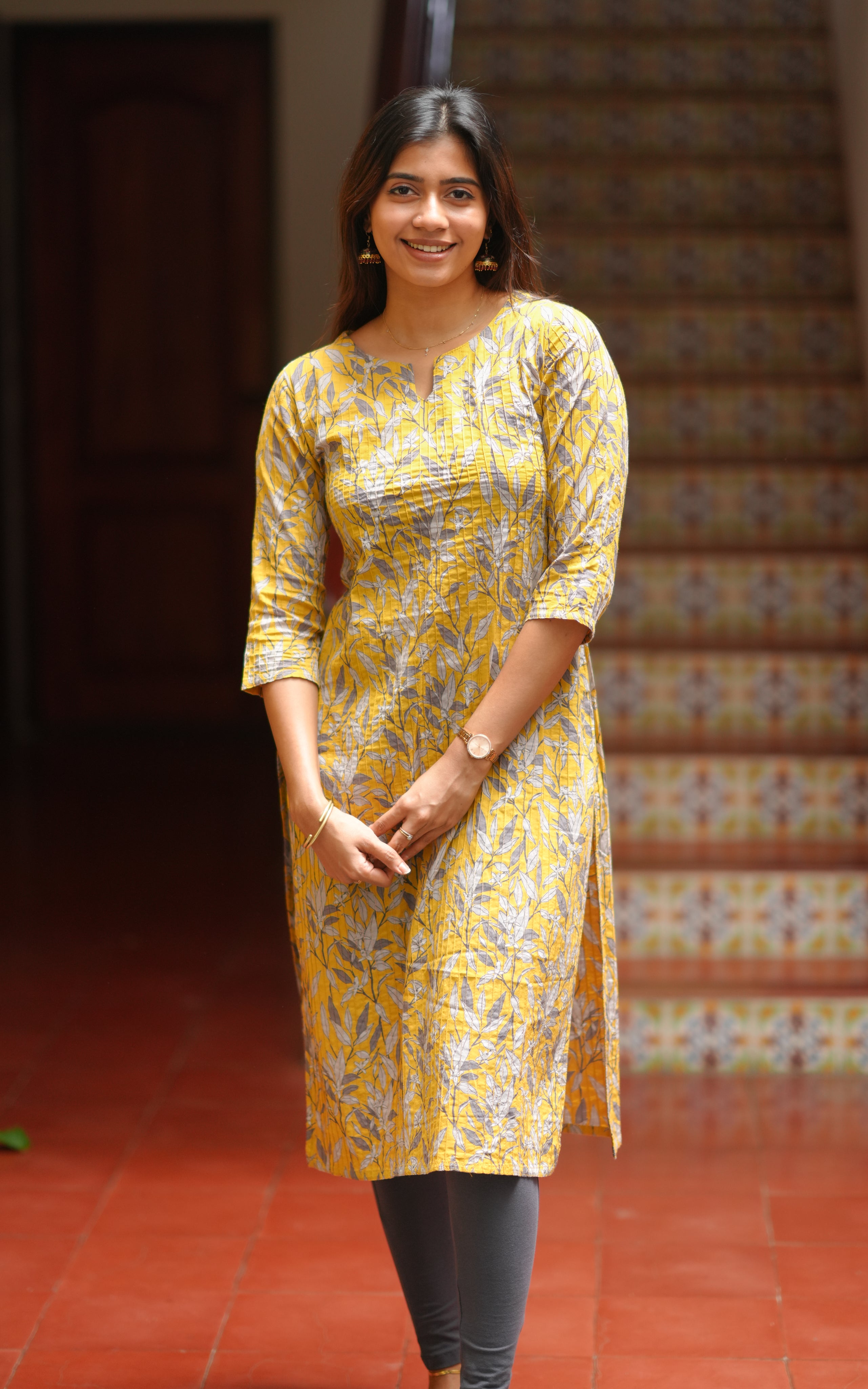 A woman is wearing a bright yellow straight-cut kurti with an all-over printed leaf pattern.