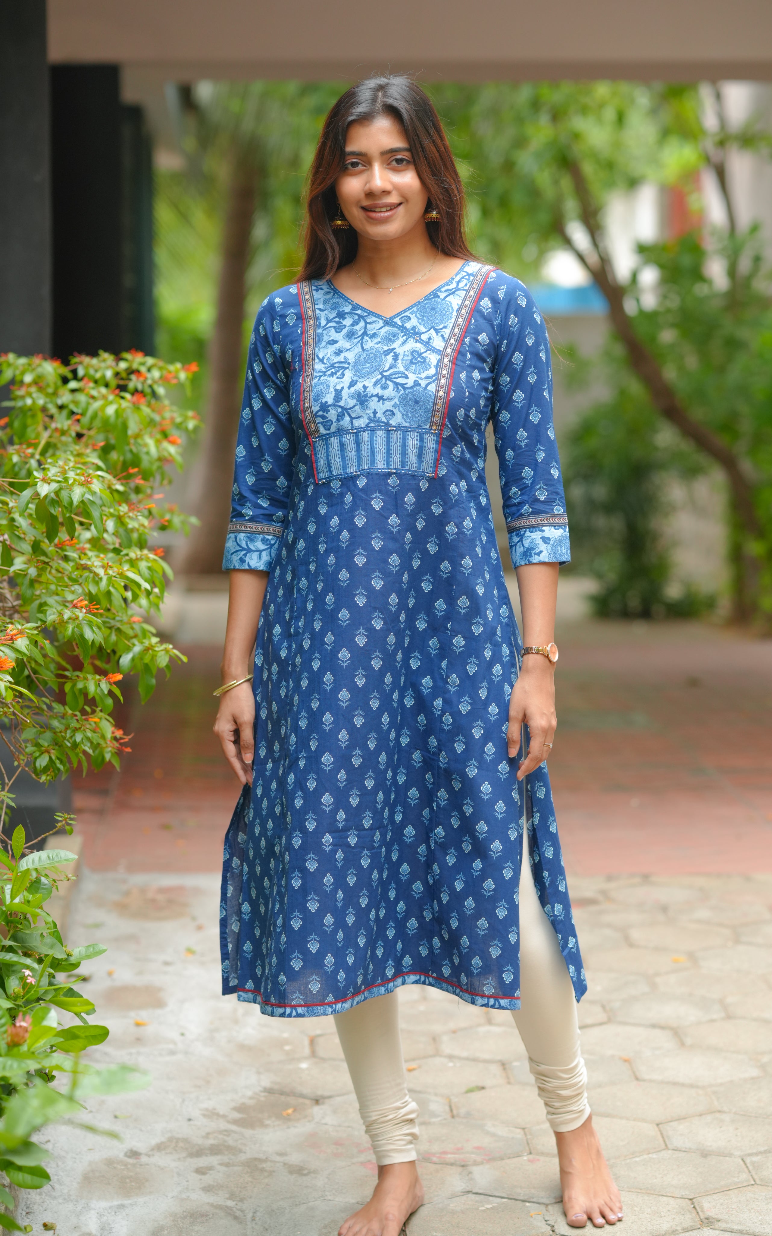 A woman is wearing an indigo blue A-line kurti with traditional handblock prints.The kurti features a V-neckline with a beautifully printed yoke in lighter blue tones.