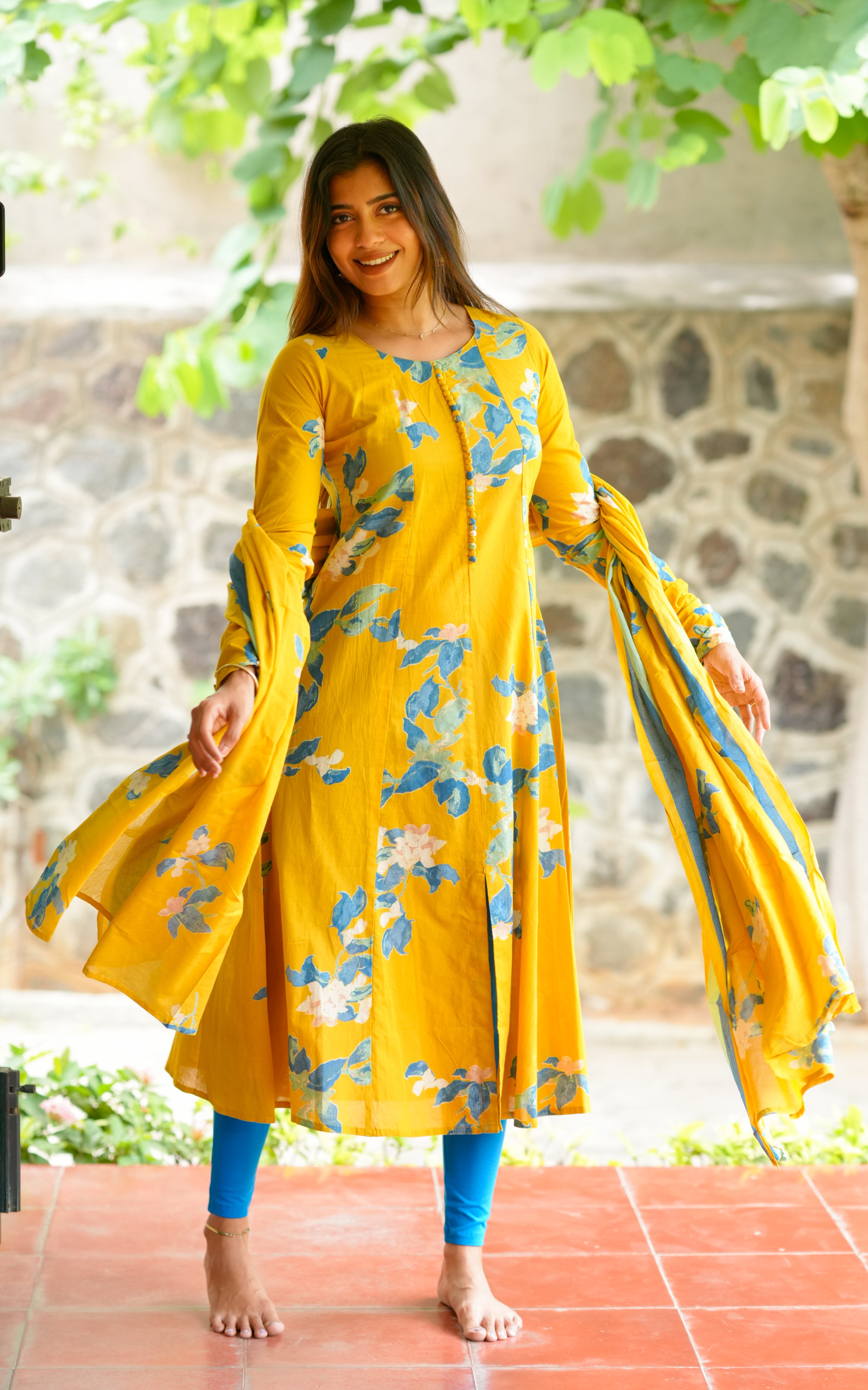 A woman is wearing a mustard yellow A-line kurti with a beautiful blue and white floral print.