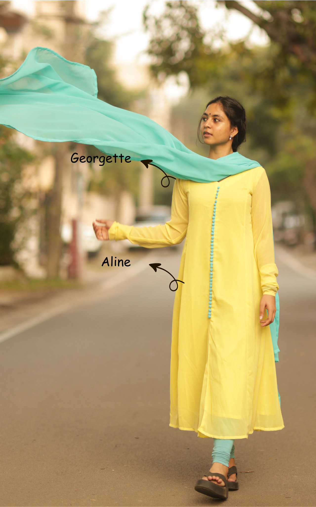 Woman wearing a yellow outfit with a blue dupatta on a road with trees in the background