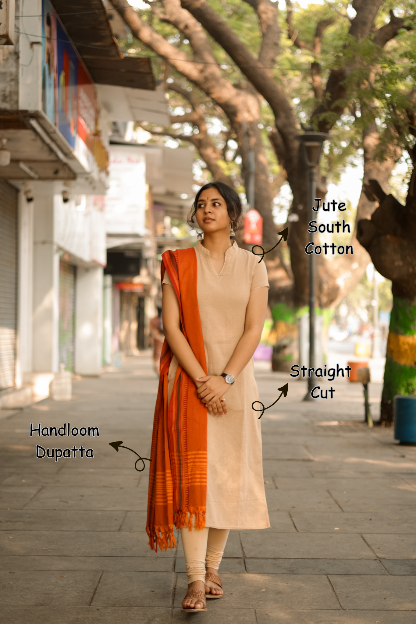 Woman in a beige kurta with an orange dupatta walking on a street.